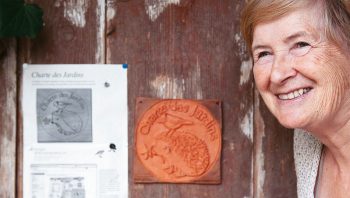 Thérèse Schwab devant une plaquette en terre cuite de "Charte des jardins" façonnée à la main par ses soins.