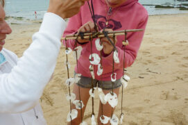Attachez les deux morceaux de bois à angle droit avec la dernière algue, en gardant une longueur libre pour accrocher le carillon. Fixez les chapelets de coquillages à la croix ainsi formée.